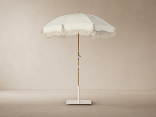Front view of a cream patio umbrella with fringe trim, a wooden pole, and a white square base.