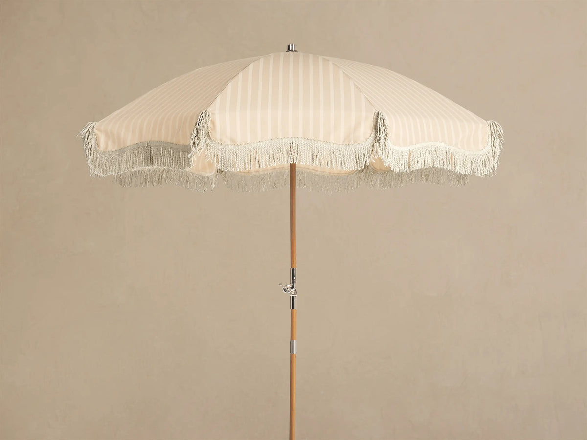 Front view of a cream and white striped parasol with a cream fringe and a light wood pole.