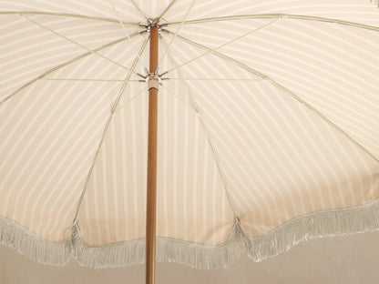 Underside view of a beige and white striped parasol with a wooden pole, metal spokes, and a light-colored fringe border.
