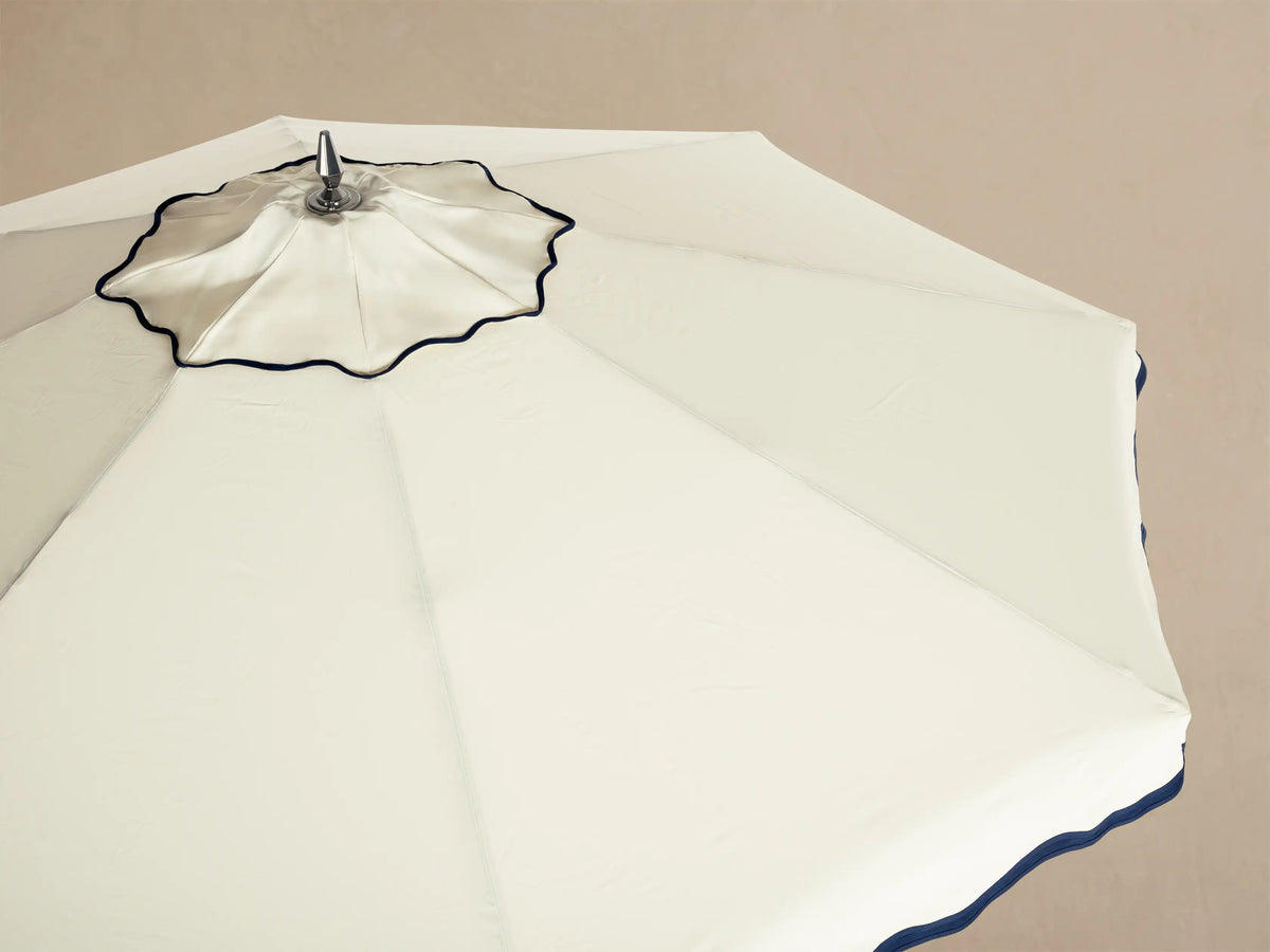 Underside view of a beige Outdoor Umbrella showing wooden pole, chrome hardware, radial spokes, and a navy blue scalloped edge.
