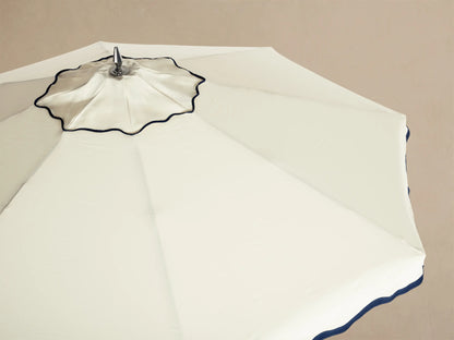 Underside view of a beige Outdoor Umbrella showing wooden pole, chrome hardware, radial spokes, and a navy blue scalloped edge.