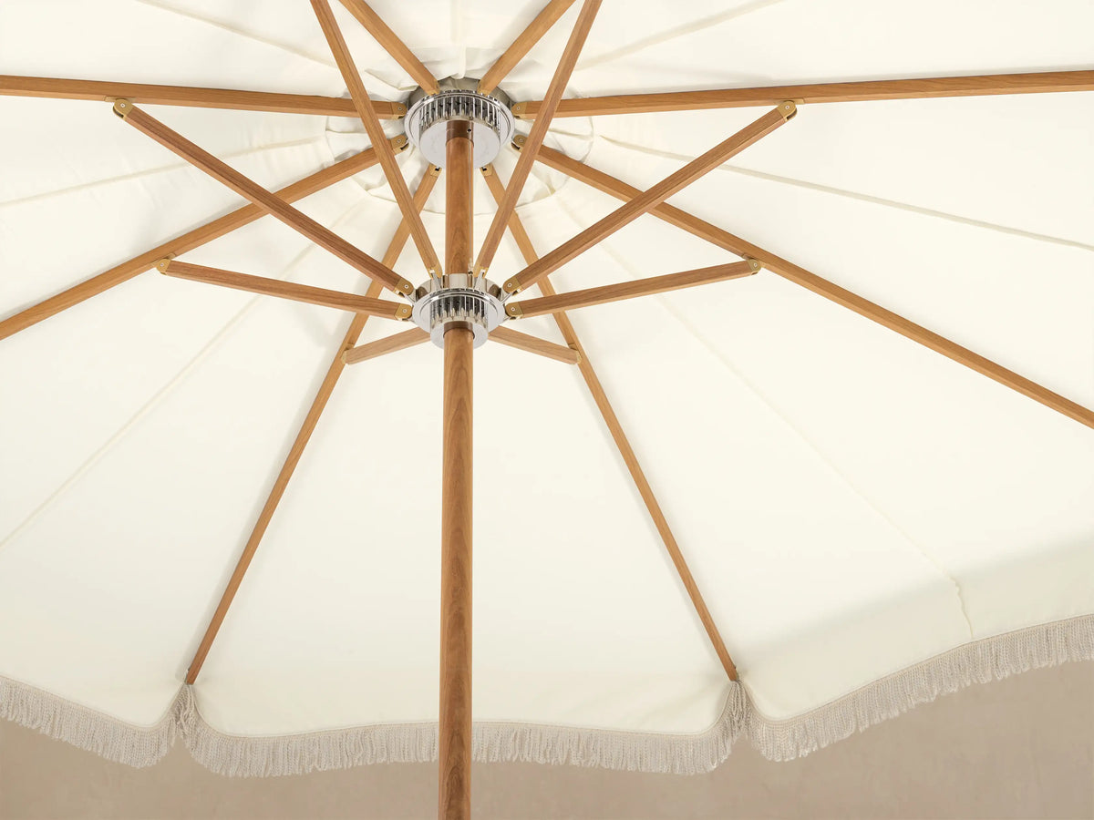 Front view of a cream patio umbrella with decorative fringe, a wooden pole, and a white base.