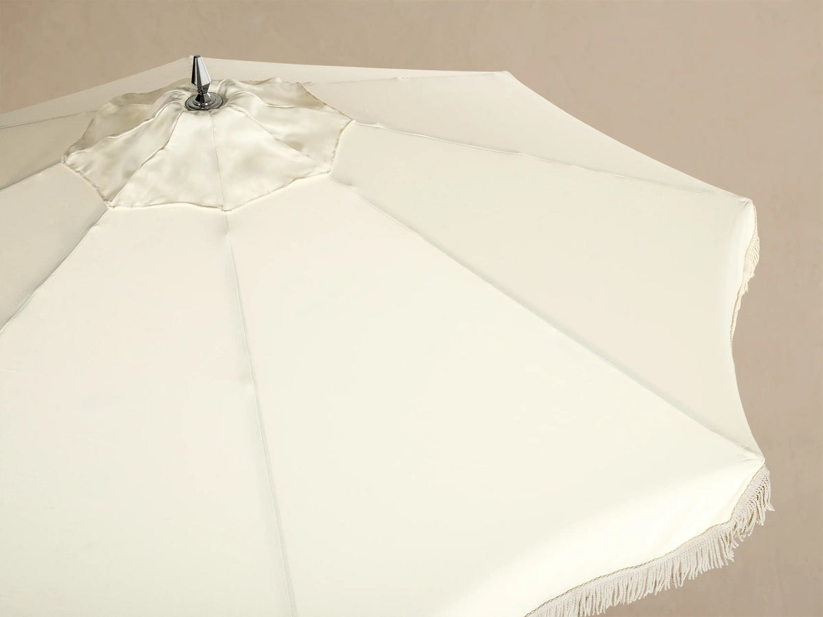 Interior view of a cream patio umbrella, showcasing its wooden frame, silver hardware, and matching fringe trim.