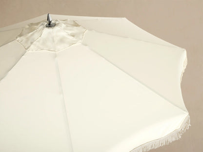 Interior view of a cream patio umbrella, showcasing its wooden frame, silver hardware, and matching fringe trim.