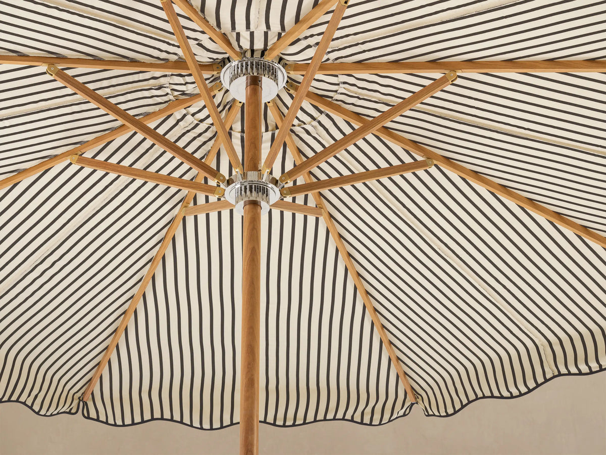 Front view of an open cream and black striped patio umbrella with a scalloped canopy, light wood pole, and white scalloped base.