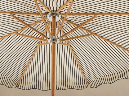Front view of an open cream and black striped patio umbrella with a scalloped canopy, light wood pole, and white scalloped base.