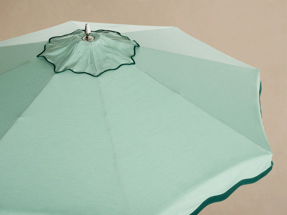Interior view of an open light green patio umbrella, showing the white frame and dark green scalloped trim.