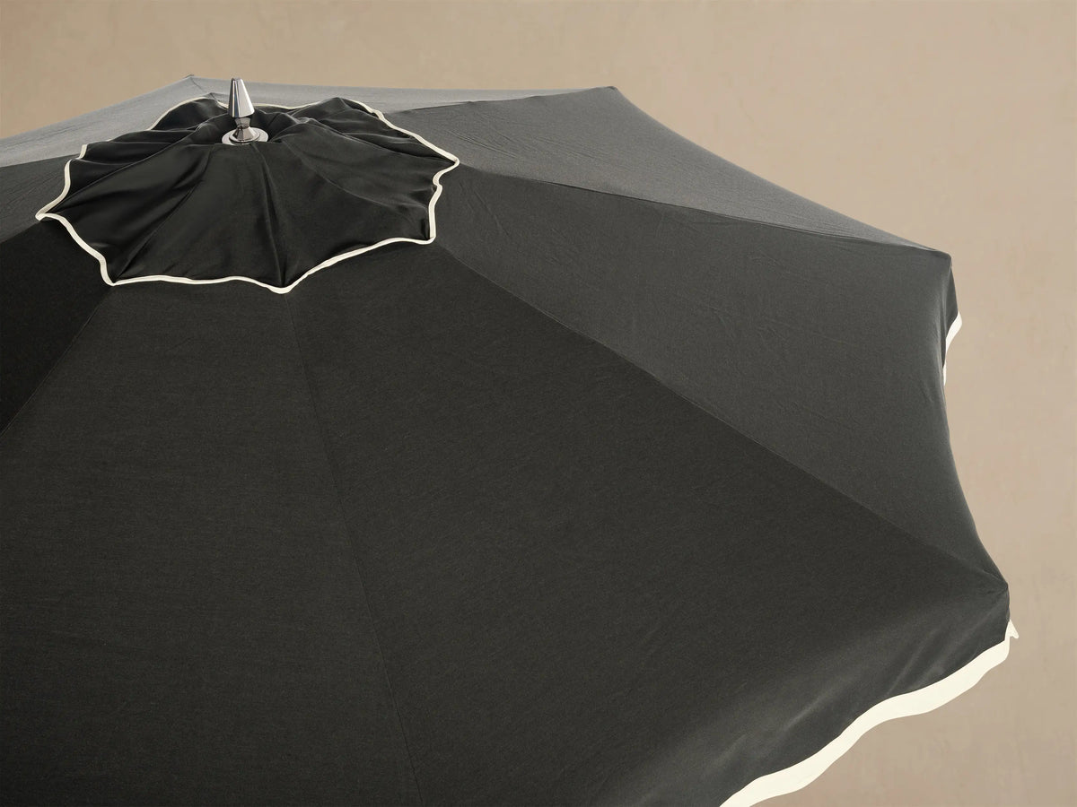 Underside view of a dark gray patio umbrella with a white frame and central pole. It has a white scalloped edge.