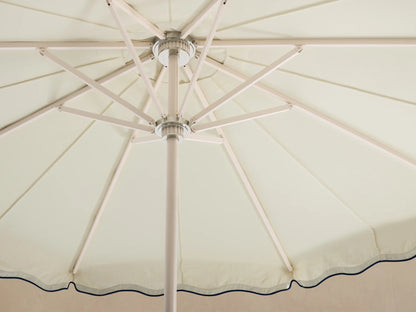 Front view of a cream patio umbrella with a scalloped edge and navy wavy trim on the canopy. White pole and base.
