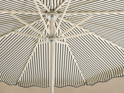 Front view of a cream and black vertically striped patio umbrella with a scalloped edge and a white pole and base.