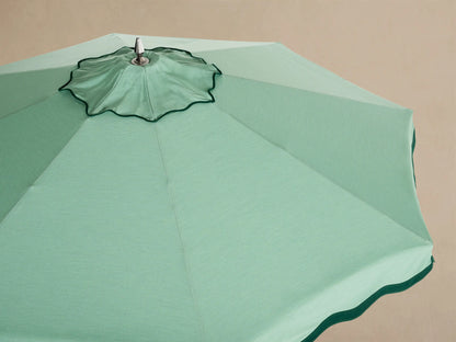Interior view of a light green patio umbrella with wooden ribs, central pole, and scalloped edge.