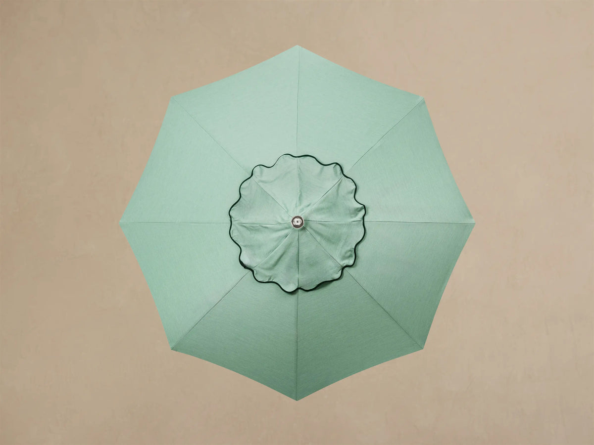 Close-up of cream outdoor umbrella base. It features a round, layered base with three metallic feet, and a pole that transitions from cream to wood.