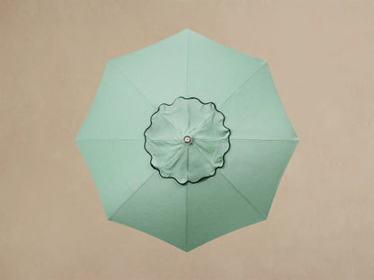 Close-up of cream outdoor umbrella base. It features a round, layered base with three metallic feet, and a pole that transitions from cream to wood.