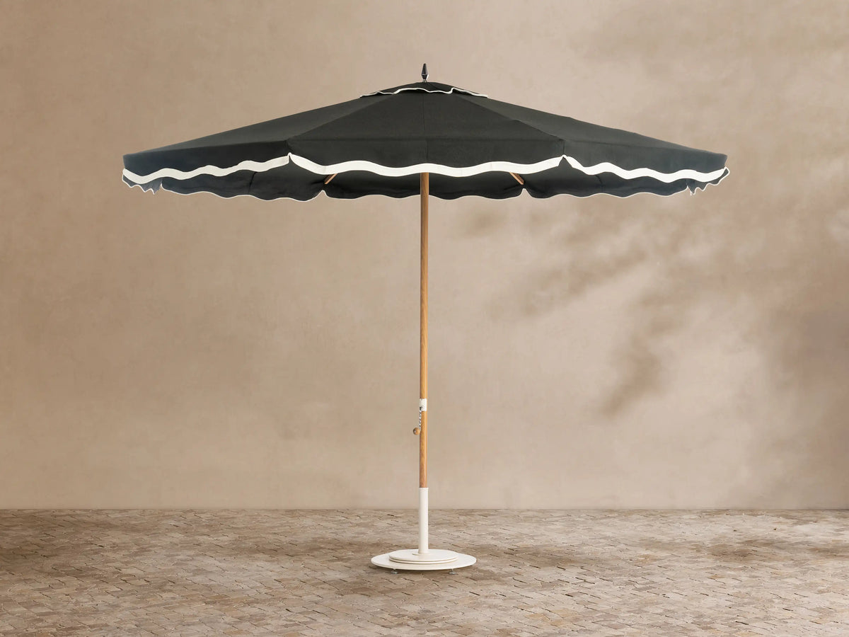 Front view of a black outdoor umbrella with white scalloped trim, a light wood pole, and a white base.