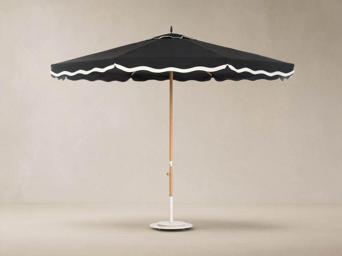 Front view of a black outdoor umbrella with white scalloped trim, a light wood pole, and a white base.