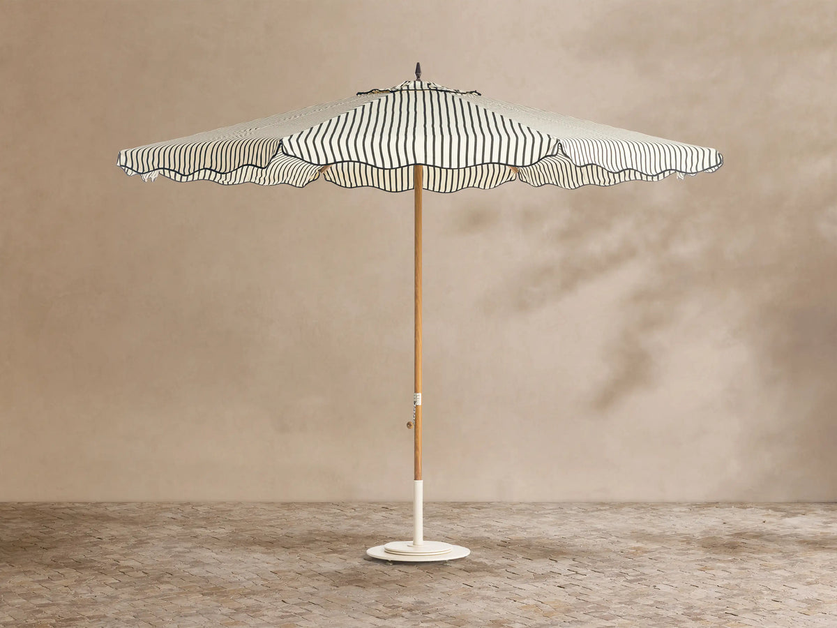 Front view of a cream and black striped patio umbrella with a scalloped edge, wooden pole, and white base.