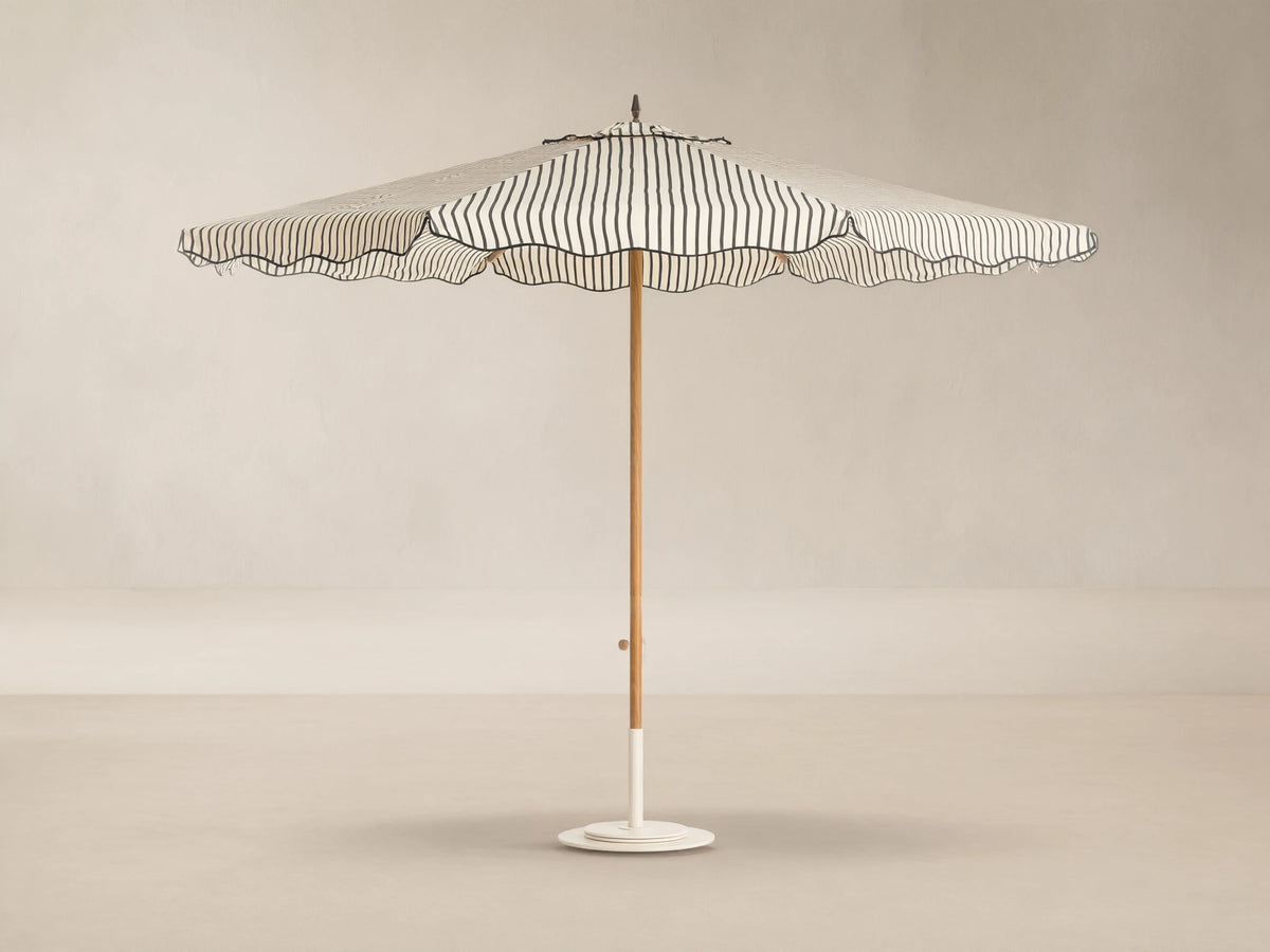 Front view of a cream and black striped patio umbrella with a scalloped edge, wooden pole, and white base.