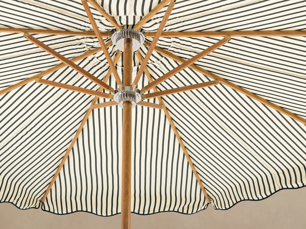 Front view of a cream and black striped patio umbrella with a scalloped edge, wooden pole, and white base.