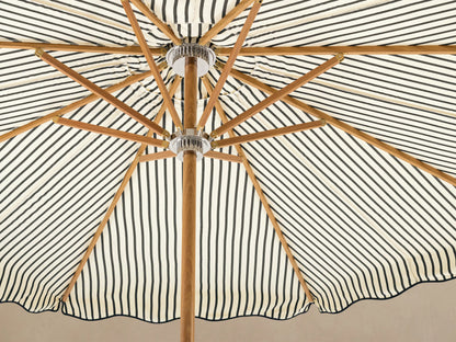 Front view of a cream and black striped patio umbrella with a scalloped edge, wooden pole, and white base.