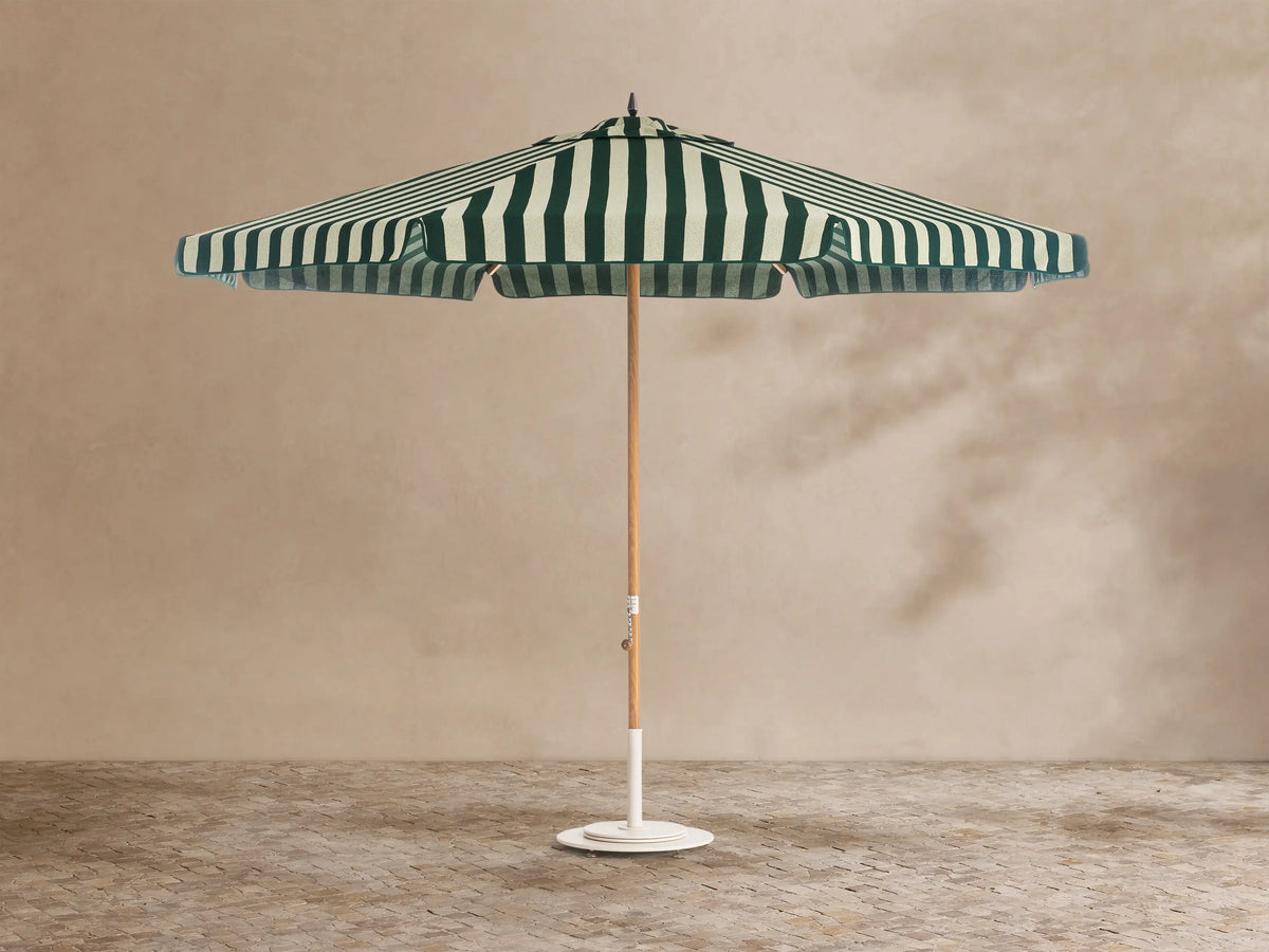 Front view of an outdoor patio umbrella with forest green and off-white vertical stripes, a natural wood pole, and a round white base.