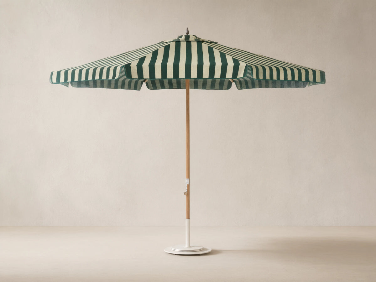 Front view of an outdoor patio umbrella with forest green and off-white vertical stripes, a natural wood pole, and a round white base.
