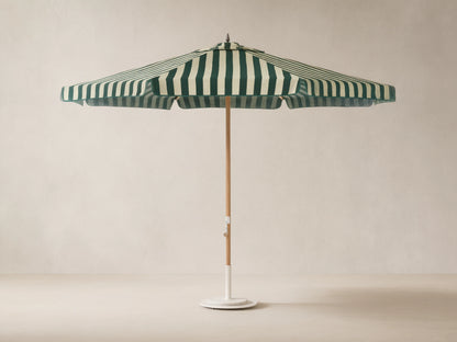 Front view of an outdoor patio umbrella with forest green and off-white vertical stripes, a natural wood pole, and a round white base.