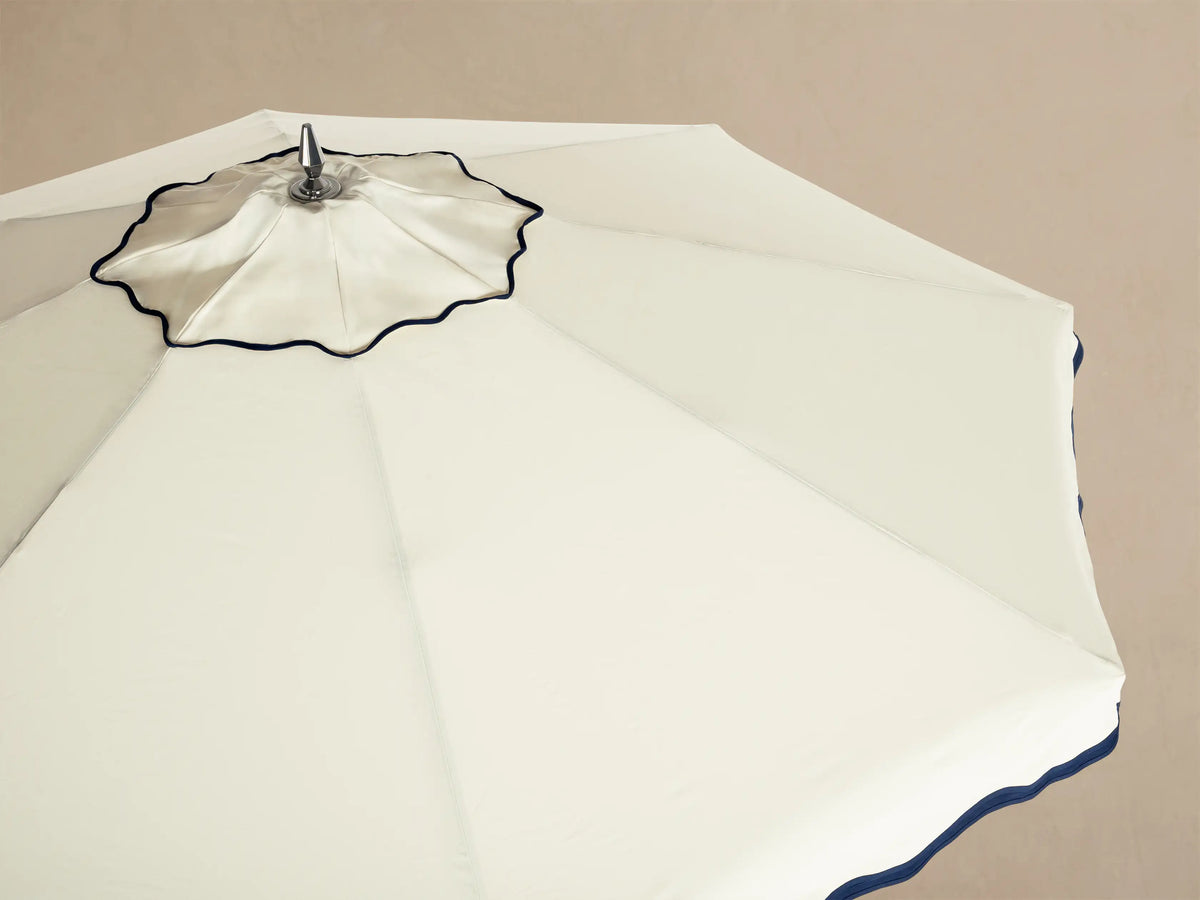 Overhead view of a cream patio umbrella with navy blue scalloped trim and a silver finial at the center.