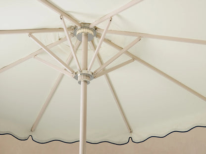 Interior view of an open cream umbrella with light tan ribs, a silver hub, and a scalloped edge with navy trim.
