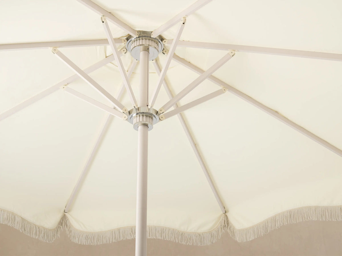 Close-up of the cream-colored round base and lower pole of a standing fixture, with three metallic support feet.