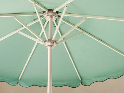 Front view of a light green patio umbrella with a dark green wavy trim, scalloped edge, white pole, and round base.