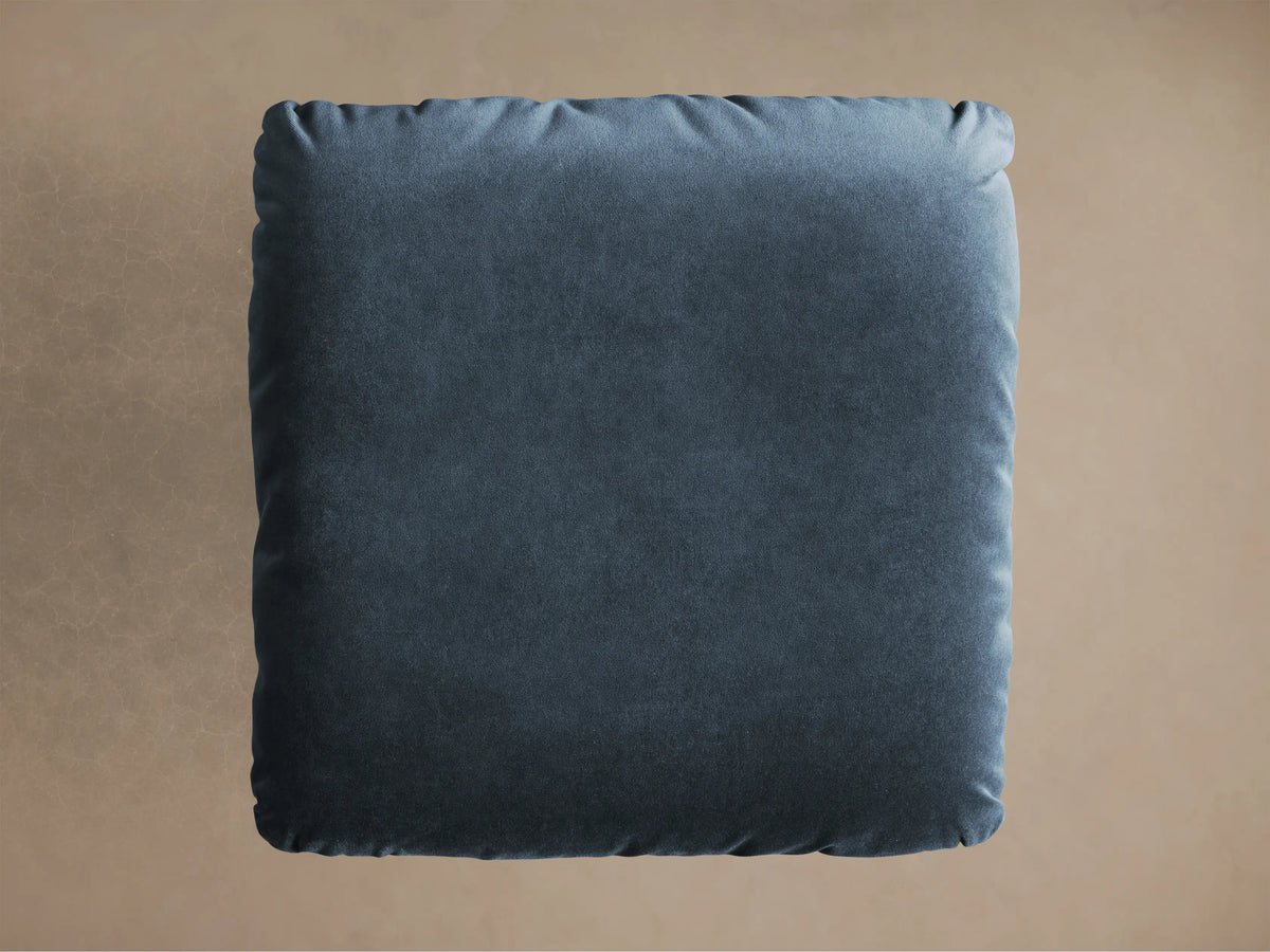Close-up of the deep teal velvet cushion and brushed silver steel base of the Deacon Ottoman.