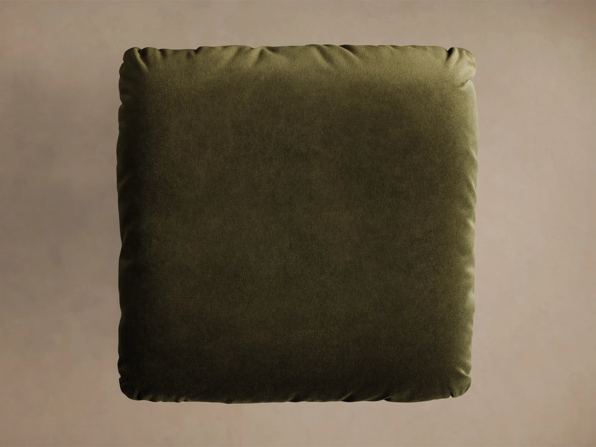 Close-up of the olive green velvet cushion and round brushed metal base of the Deacon Ottoman.