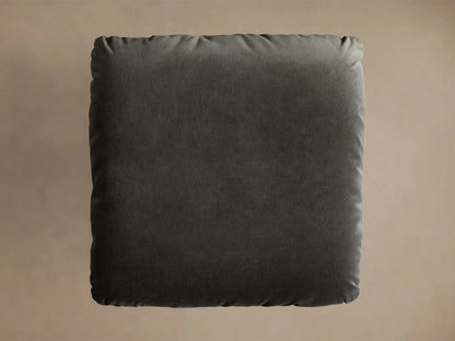 Front view of the charcoal Deacon Ottoman, featuring a plush cushion and a brushed metal pedestal base.