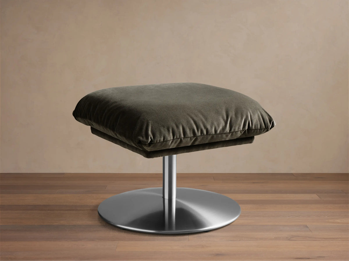 Front view of the dark green cushioned Deacon Ottoman with a circular silver metallic base.