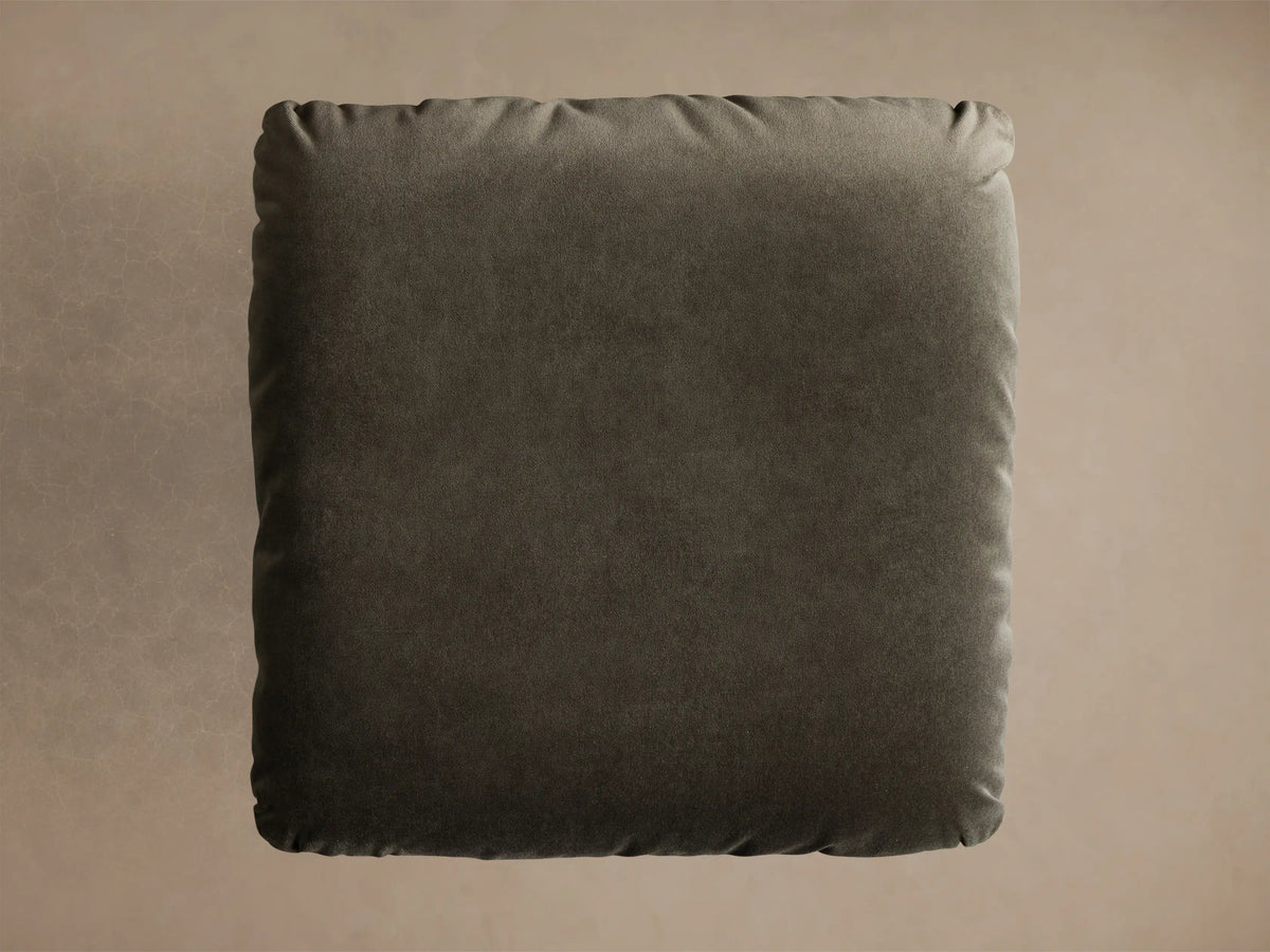 Close-up, angled view of the Deacon Ottoman with a dark olive plush cushion on a brushed silver circular base.