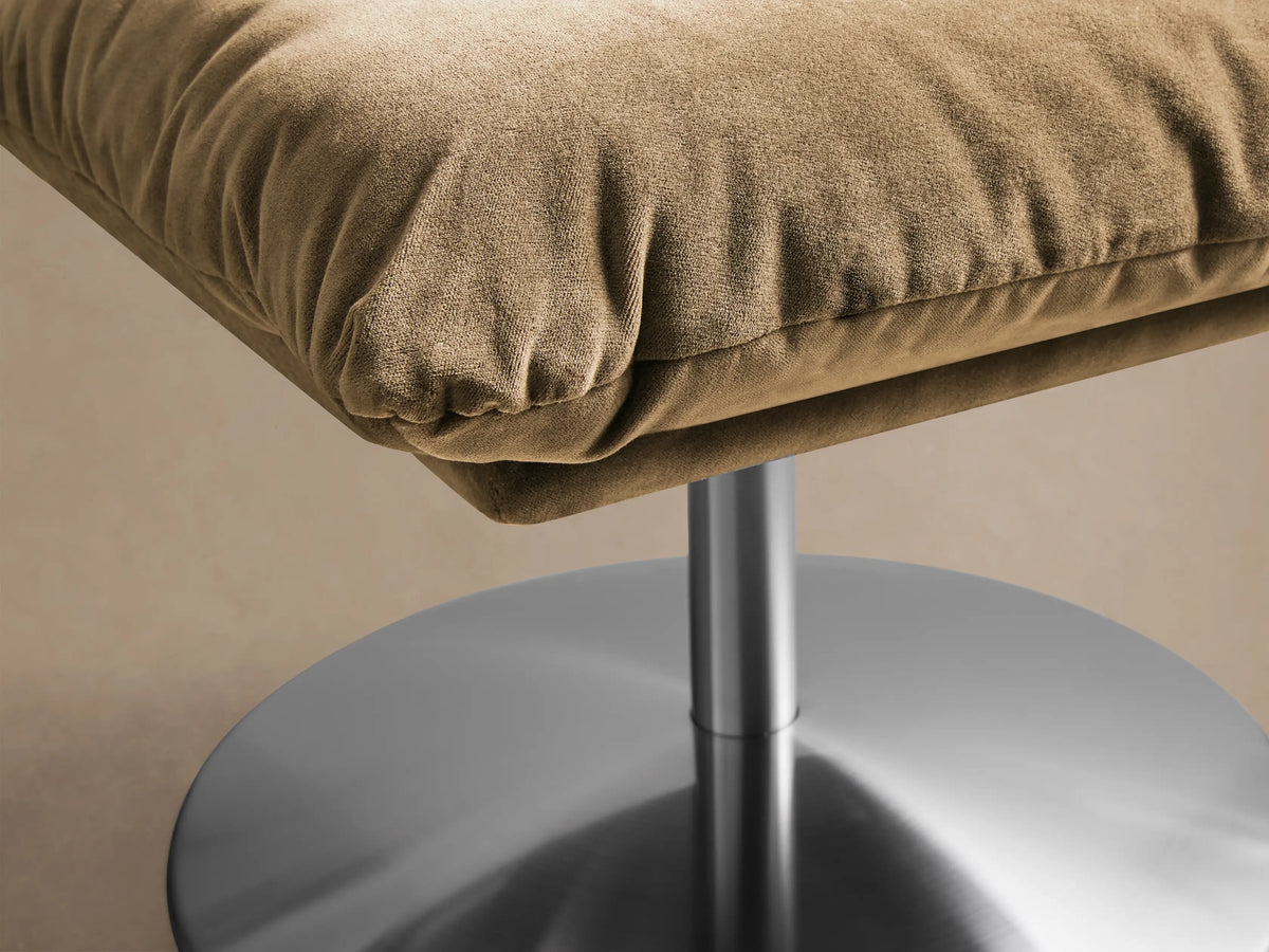 Front view of a camel Deacon Ottoman with a plush cushion, supported by a silver cylindrical post and round base.