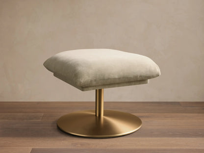 Front view of the cream Deacon Ottoman, featuring a soft padded cushion on a brushed gold pedestal base.