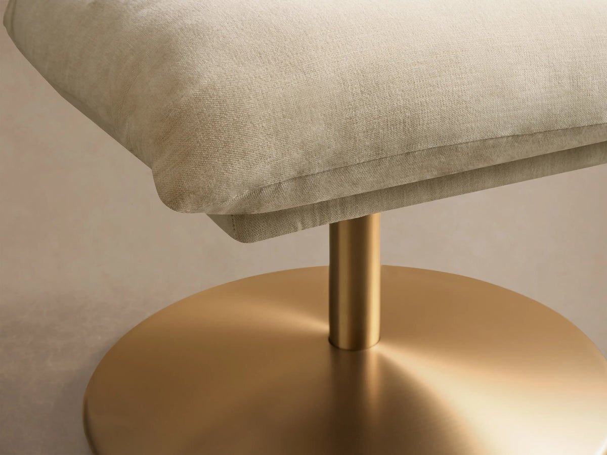 Front view of the light beige Deacon Ottoman with a soft, plump square cushion and a gleaming round gold metal base.