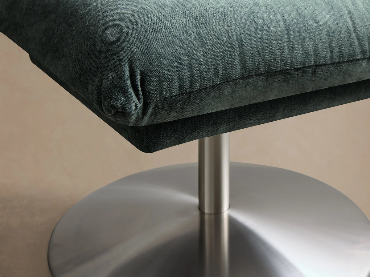 Teal green Deacon Ottoman with a plush square cushion on a brushed steel pedestal base, shown in a 3/4 view.