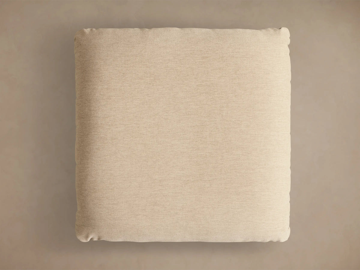 Close-up of the beige upholstered cushion on a gold metallic base of the Deacon Ottoman.