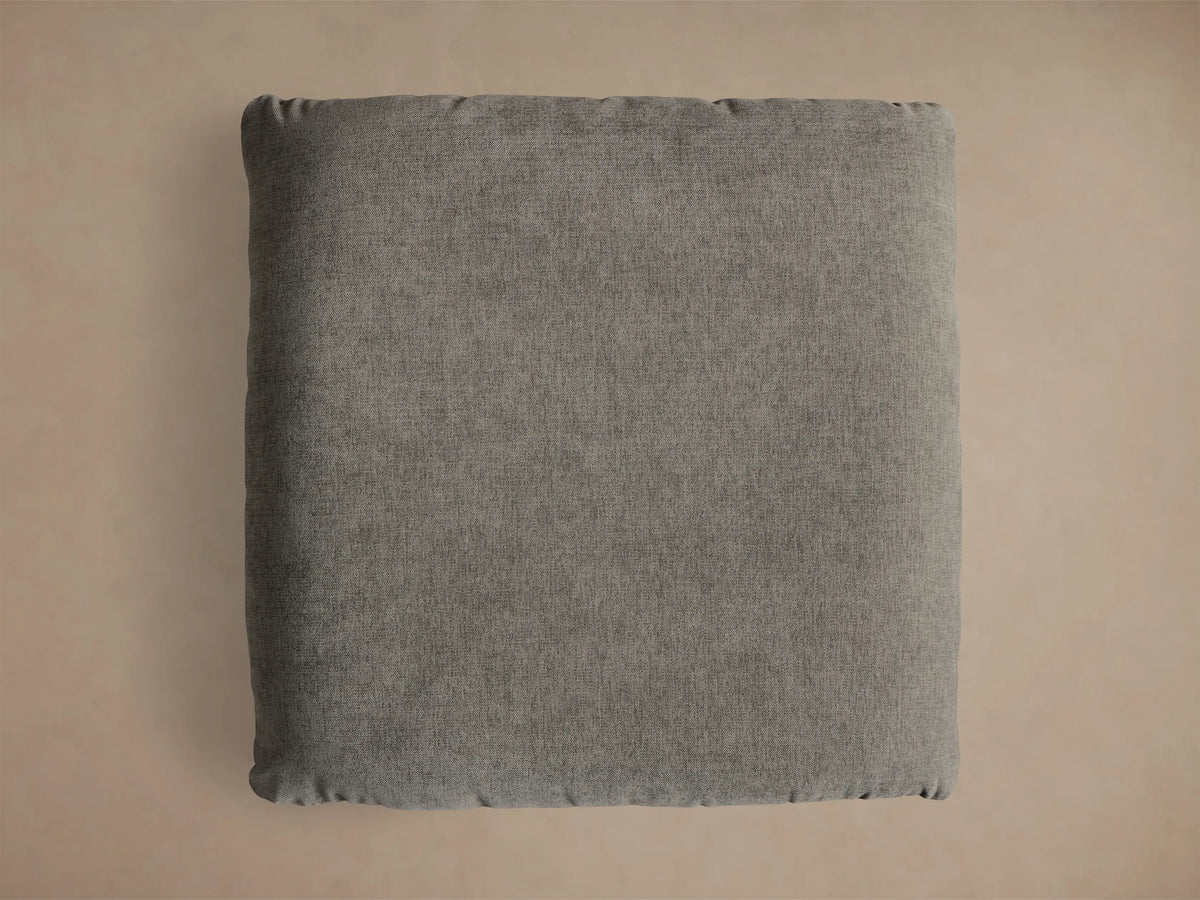 Close-up of the charcoal Deacon Ottoman with a textured cushion resting on a round, brushed silver steel base.