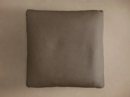 Front view of the taupe leather Deacon Leather Ottoman with a plump cushion and black circular pedestal base.