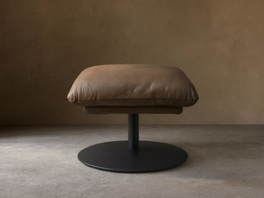 Front view of the taupe leather Deacon Leather Ottoman with a plump cushion and black circular pedestal base.