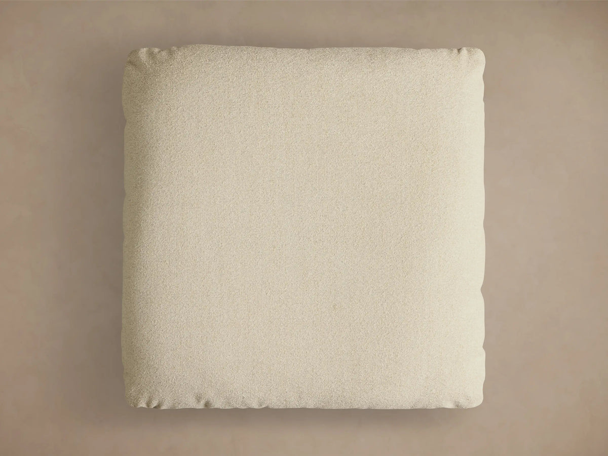 Close-up of the beige textured cushion, silver cylindrical support, and round brushed metal base of the Deacon Ottoman.
