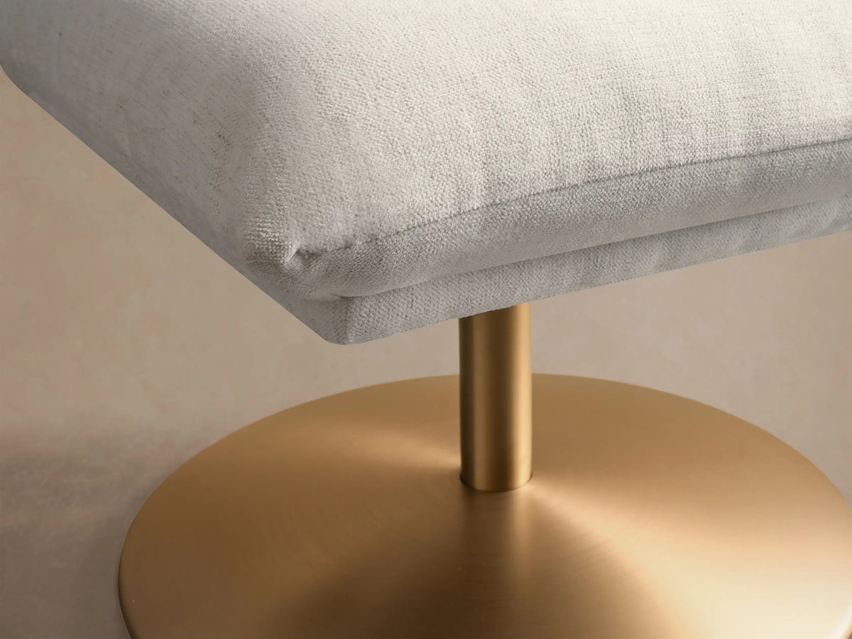 Side view of a light cream Deacon Ottoman with a square cushion and a round, matte gold base.