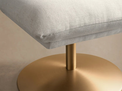 Side view of a light cream Deacon Ottoman with a square cushion and a round, matte gold base.