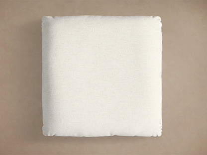 Close-up of the light beige textured cushion and circular brushed gold base of the Deacon Ottoman.
