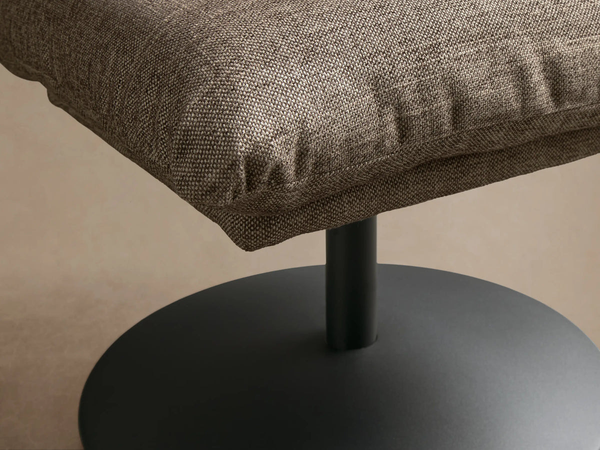 Front view of the brown-grey heathered Deacon Ottoman, featuring a plush cushion and black metal pedestal base.