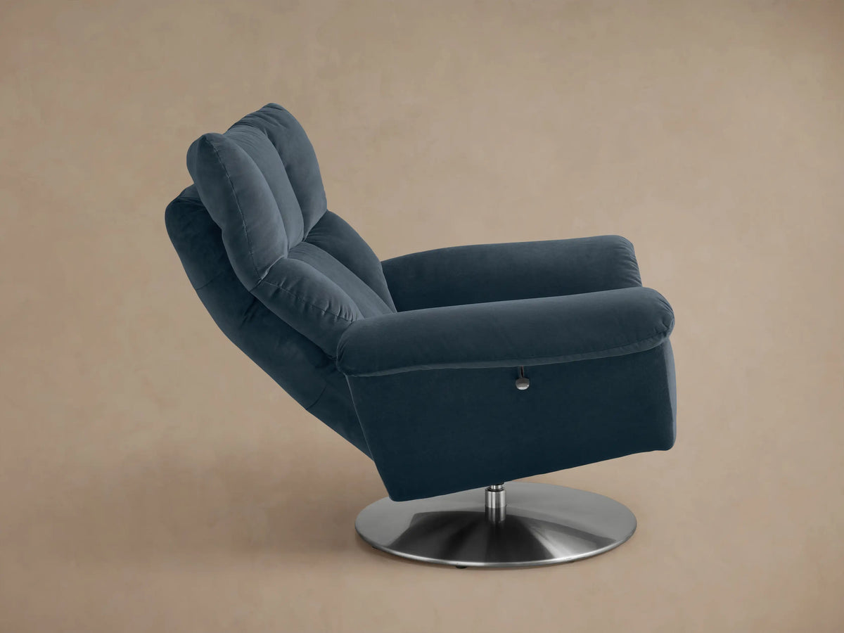 Angled rear view of a plush, dark blue Deacon Swivel Recliner with stitching details and a round silver swivel base.