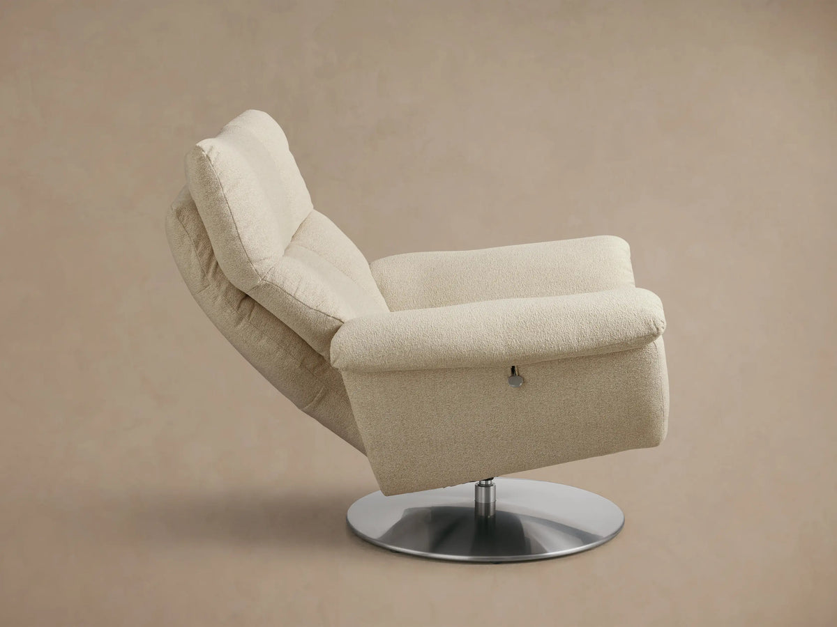 Rear three-quarter view of the light beige Deacon Swivel Recliner, featuring a plush cushioned back and armrests, and silver swivel base.